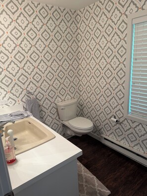 Un baño con papel tapiz estampado, un inodoro, un lavabo y una ventana con persianas.
