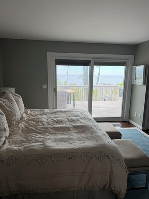 Un dormitorio con una cama grande, un banco y un ventanal corredera que da a un balcón con vistas al mar.