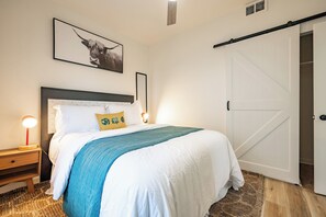 Ein Schlafzimmer mit einem Bett, Nachttischen, einem Wandbild, einer Schiebetür und einem Strukturteppich.