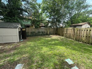 A fenced backyard with a shed, a small house, and trees.
