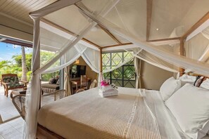 Ein Schlafzimmer mit Baldachinbett, Korbmöbeln und Blick auf Grünflächen.
