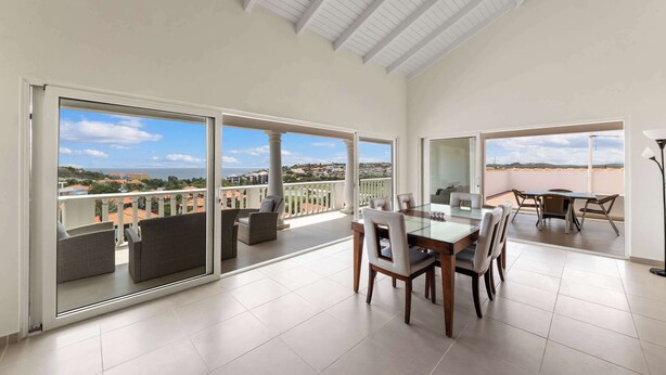 A spacious balcony with a dining area, large sliding glass doors, and a view of the cityscape.