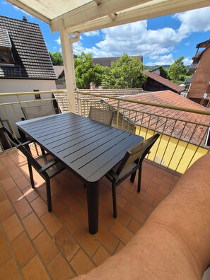 Ein Balkon mit Tisch und Stühlen, einem gelben Geländer und Blick auf benachbarte Gebäude und Bäume.
