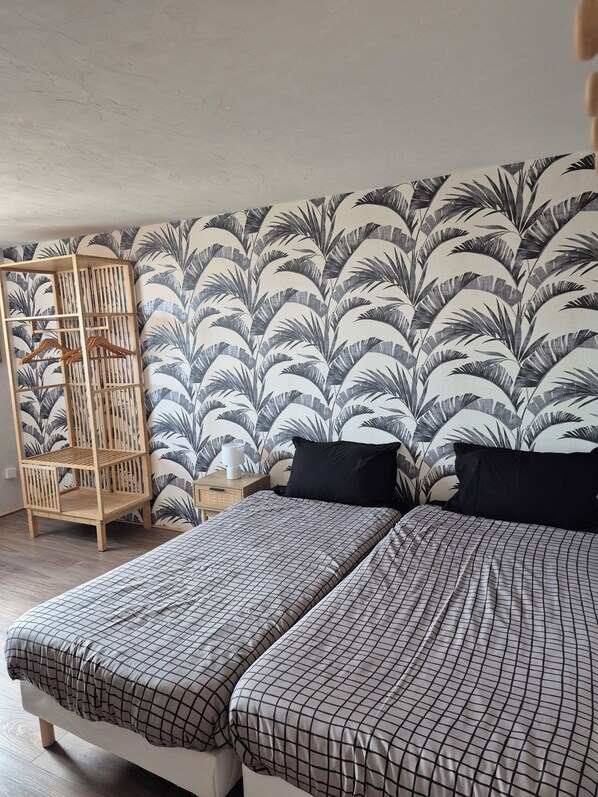 Ein Schlafzimmer mit zwei Betten, einem Holzschrank und einer Wand mit Blätermotiv.