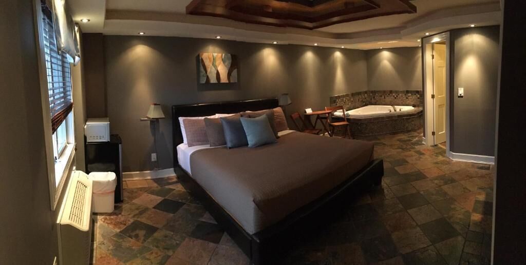 Quarto com cama grande, área de estar, banheira e escrivaninha com computador.