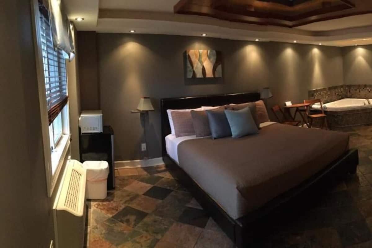 Un dormitorio con una cama grande, una zona de estar, una bañera y un escritorio con una computadora.