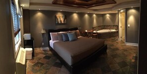 Un dormitorio con una cama grande, una zona de estar, una bañera y un escritorio con una computadora.