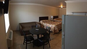 Habitación de hotel compacta con cama, una pequeña mesa de comedor con sillas, un sofá, un refrigerador y un calefactor.