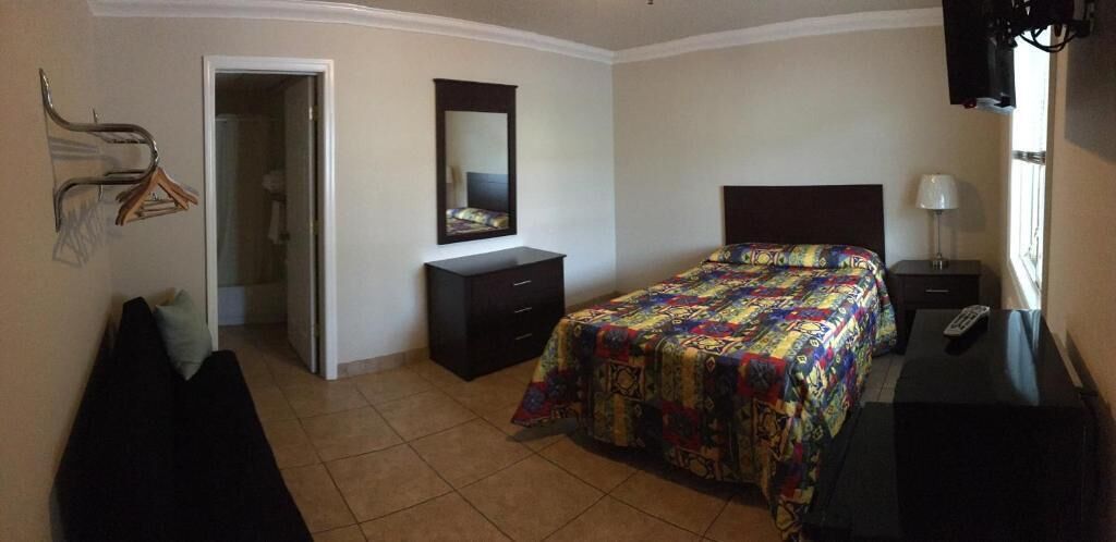 Quarto com cama, cômoda, mesa de cabeceira, espelho, televisão e porta que dá para outro espaço.