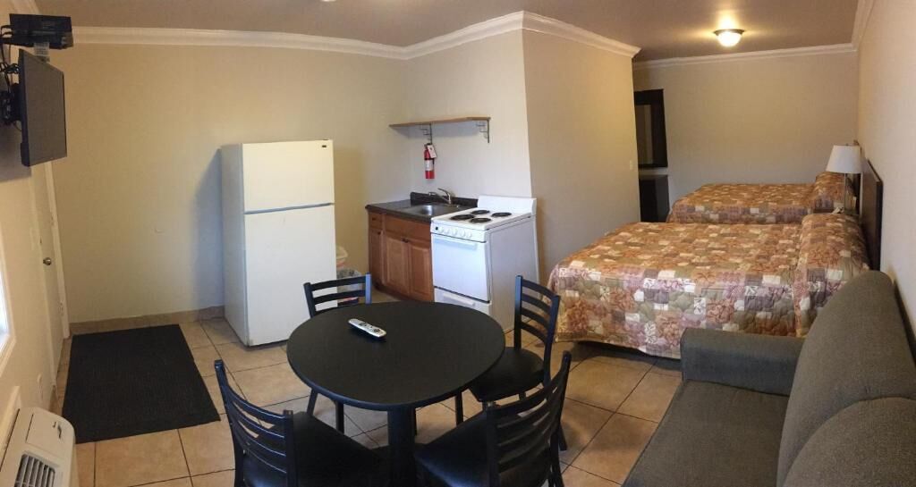 Quarto compacto com cozinha compacta, mesa de jantar com cadeiras, sofá e duas camas.