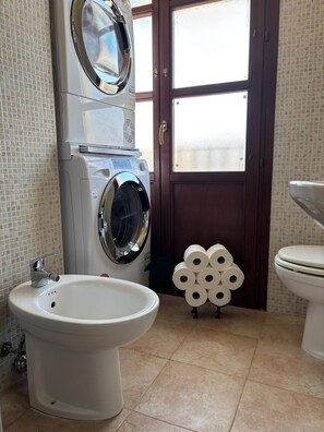 Ein Badezimmer mit Waschmaschine, Bidet, Toilette und Fliesenboden.