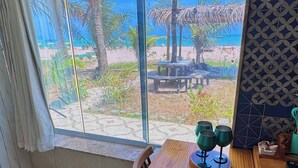 Ein Zimmer mit großem Fenster zum Strand, einem Holztisch und einem Stuhl.