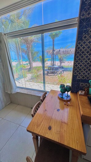 Ein Zimmer mit großem Fenster zum Strand, einem Holztisch und einem Stuhl.