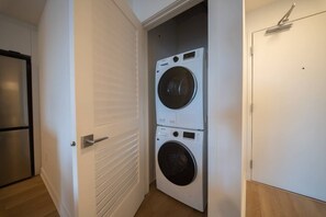 Ein Waschraum mit zwei übereinander gestapelten Waschmaschinen, einer Tür mit Griff und einem Lichtschalter an der Wand.