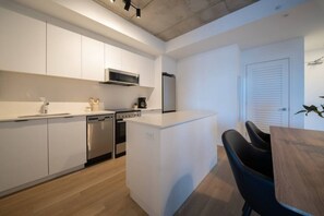 A modern kitchen with white cabinetry, stainless steel appliances, and a small island with a black chair.