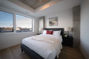 Ein modernes Schlafzimmer mit einem großen Bett, einem Nachttisch, einer Lampe und einem Fenster mit Blick.