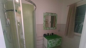 Un bany amb dutxa, un lavabo amb una estora verda i un mirall amb marc floral.
