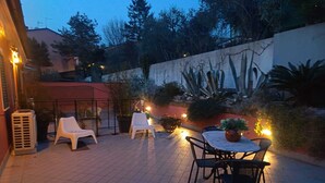 Terrassa exterior amb caires i taula, envoltada de plantes i una paret amb mural.