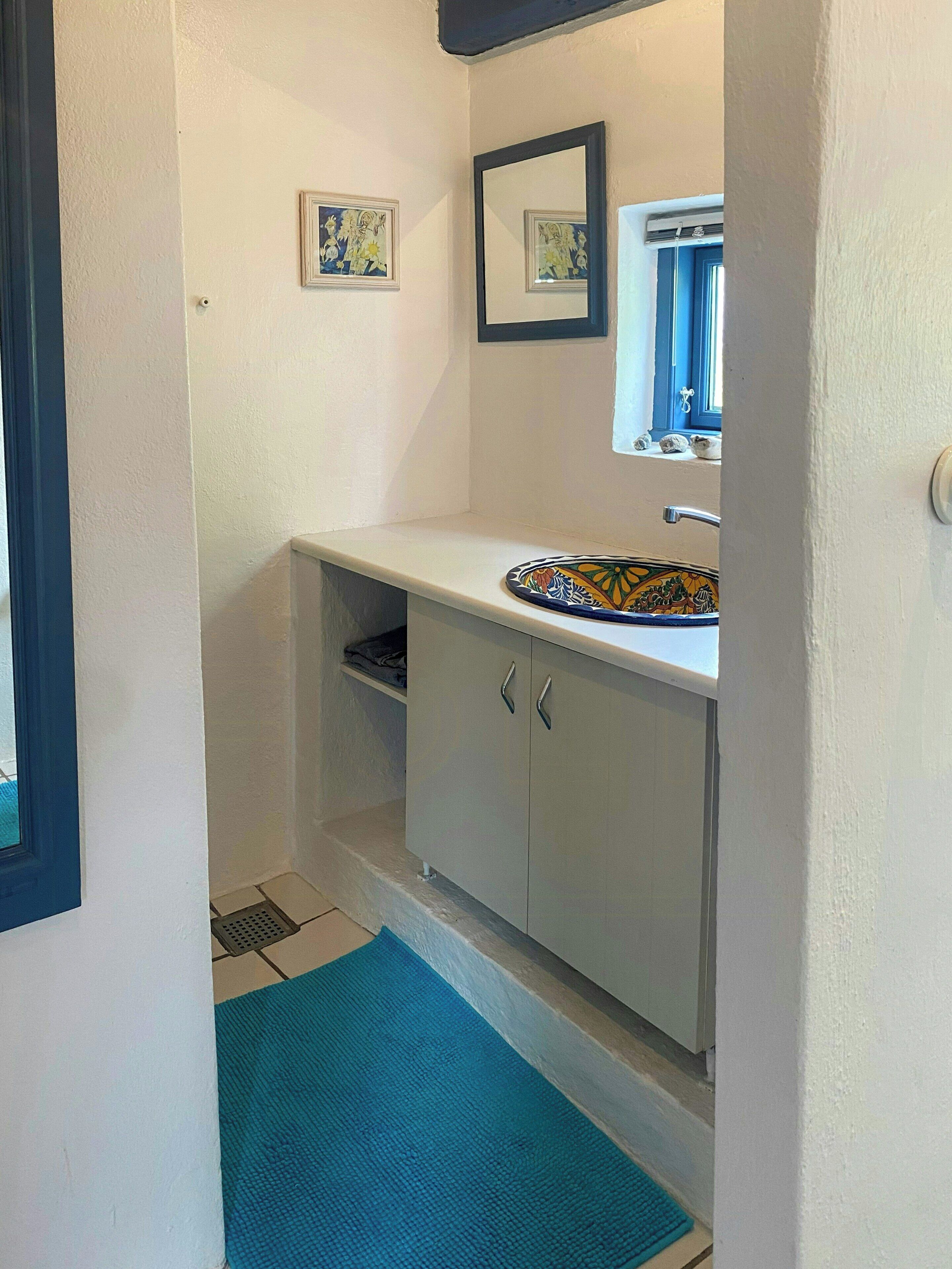 A bathroom with a white sink, a mirror, and a blue mat on the floor.