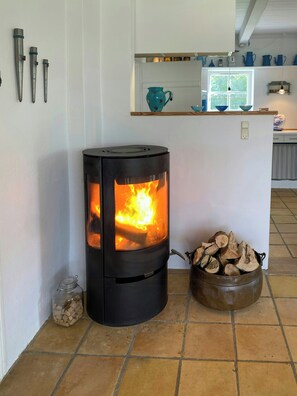 Ein Holzofen mit Feuer, ein Glasgefäß mit Holz und ein Metalltopf mit Holz auf einem Kachelboden.