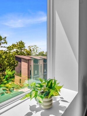 Un interior moderno con un ventanal grande, una planta en maceta y vistas de un edificio.