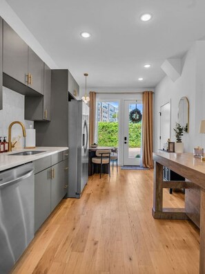 Una cocina moderna con armarios grises, una mesa de comedor de madera y vistas al exterior con vegetación.