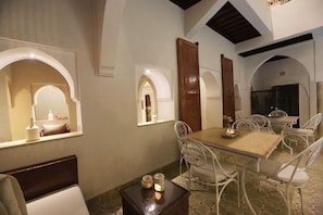 A dining area with a table and chairs, a small table with candles, and a TV in the background. - Riad Étoile du Sud (Sidi Abdallah Ghiat)