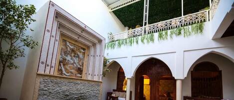 A pool with a stone wall, white arches, and a balcony with greenery.