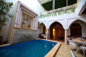 A pool with a stone wall, white arches, and a balcony with greenery. - Riad Étoile du Sud (Sidi Abdallah Ghiat)