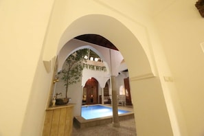 Una piscina interior amb un sostre arquejat, una banca de fusta i una planta en test.
