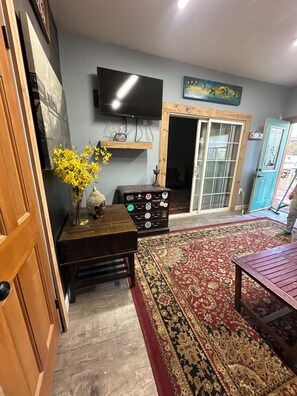 Una sala de estar con televisor, muebles de madera, alfombra estampada y una puerta azul.