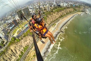 Eine Person macht Bungeesprung, gesichert mit Ausrüstung, mit Blick auf eine Küstenstadt mit Gebäuden und einem Strand.