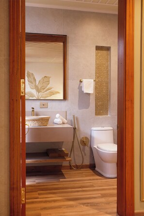 A bathroom with a wooden floor, a white sink, a toilet, and a large mirror.