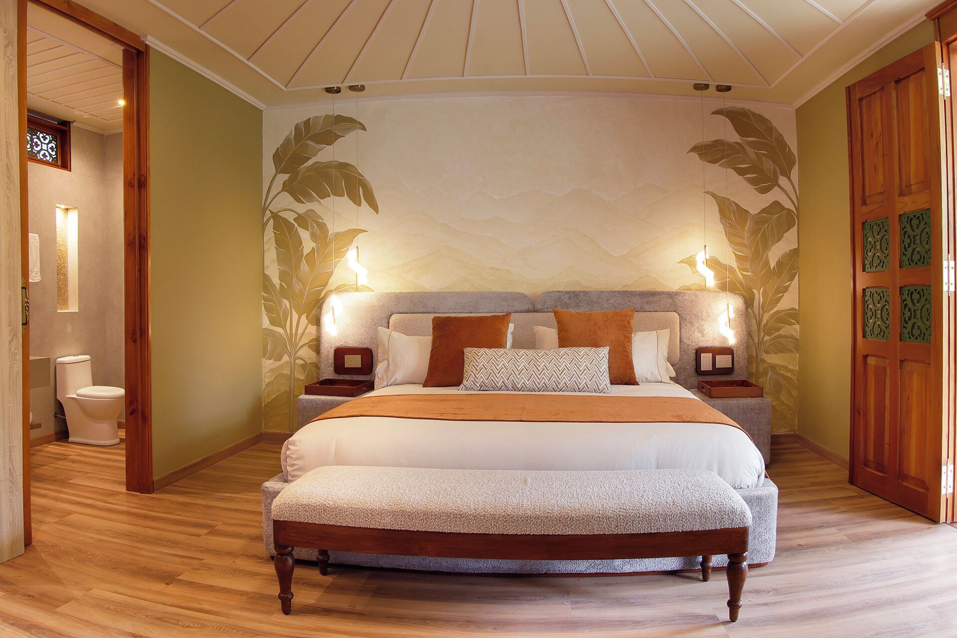 Un dormitorio con una cama grande, cabecera de madera, dos mesitas de noche con lámparas y un mural en la pared.