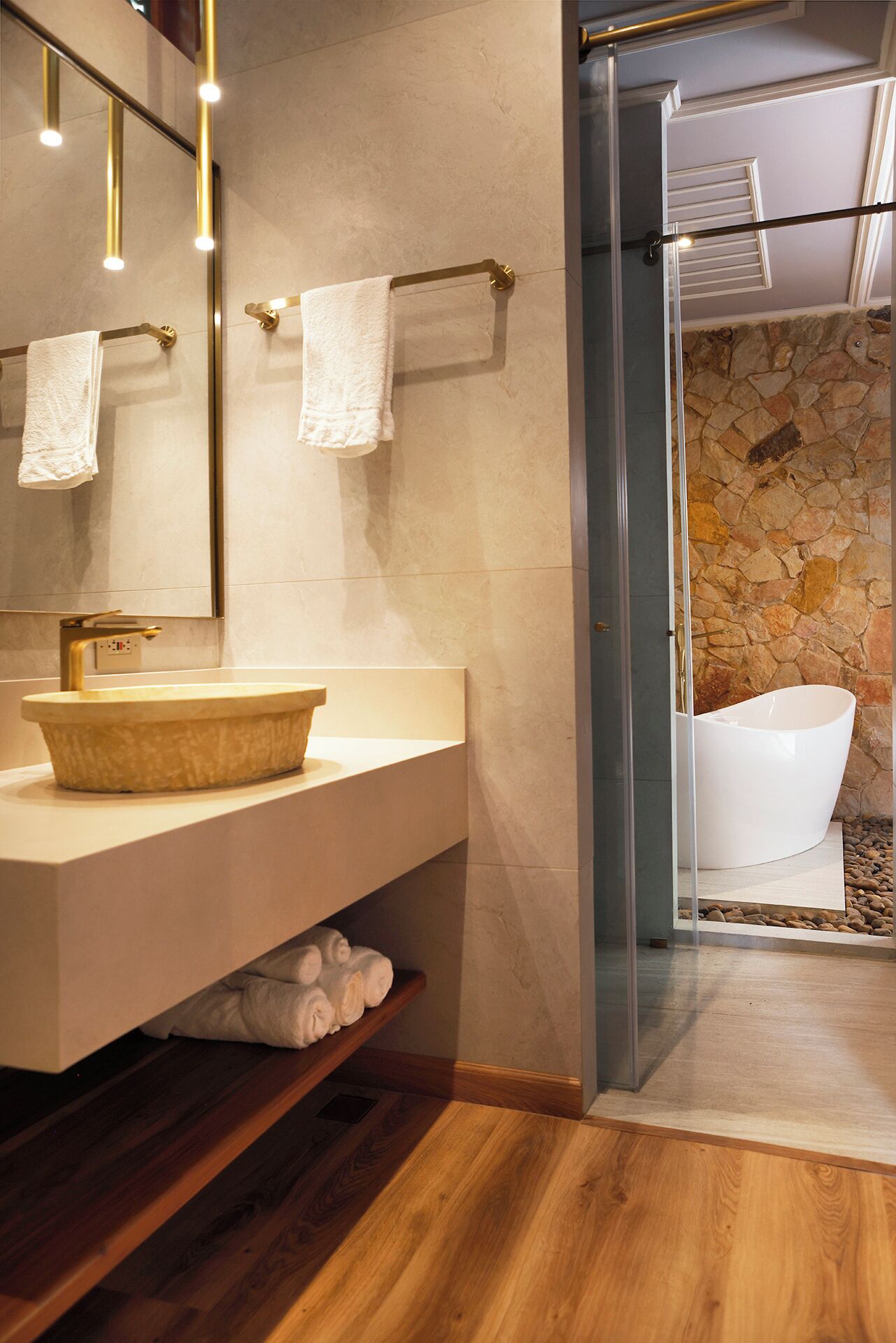 Un baño moderno con pared de piedra, tocador de madera, lavamanos grande y cabina de ducha con mampara de vidrio.
