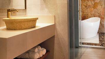 Un baño moderno con pared de piedra, tocador de madera, lavamanos grande y cabina de ducha con mampara de vidrio.