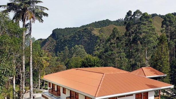 A two-story house with a red-tiled roof, white walls, and wooden balconies. - El Molino Ecohotel (Salento)