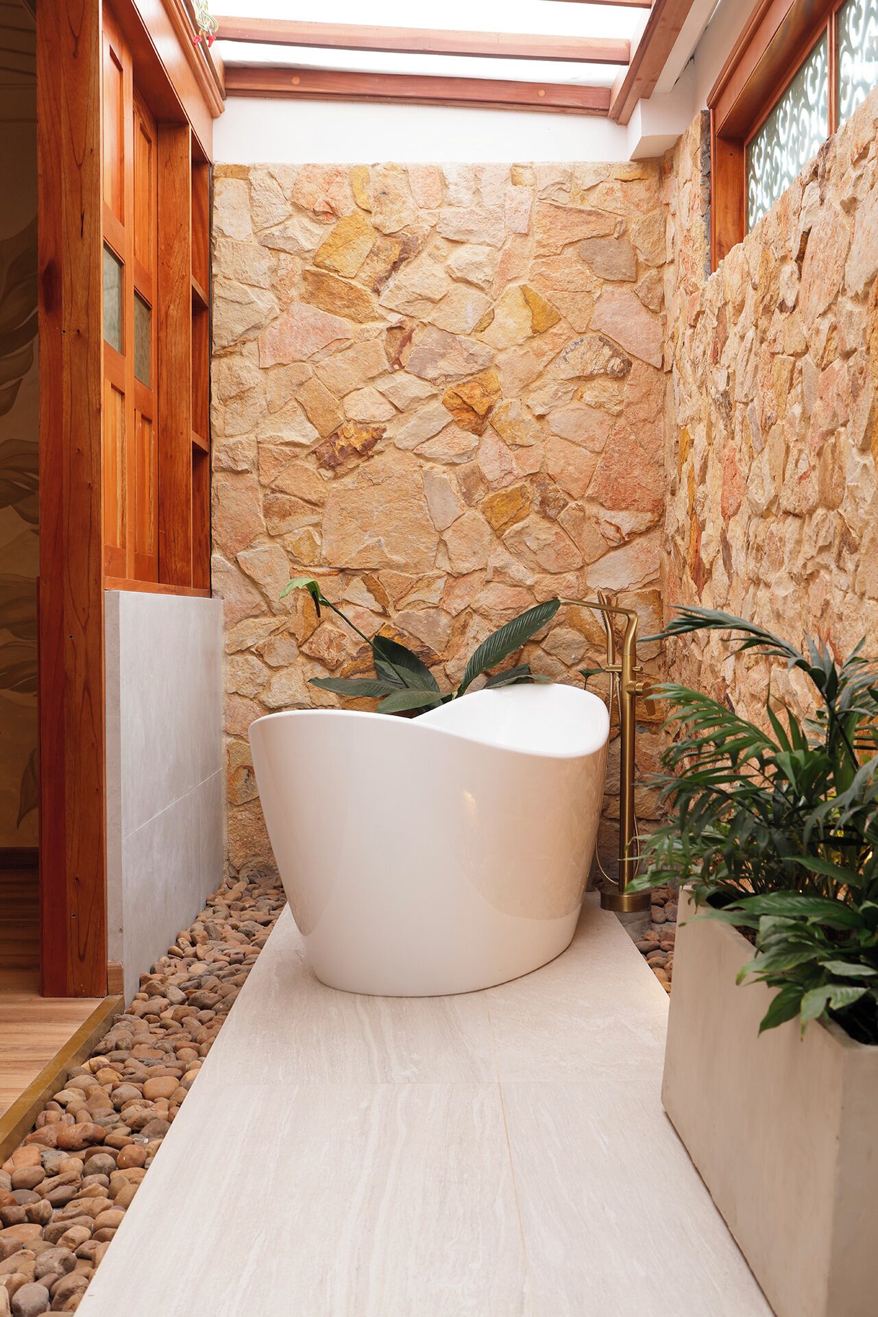 Un baño moderno con pared de piedra, una bañera independiente y plantas en macetas.