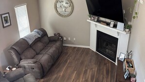A living room with a sectional sofa, a flat-screen TV, a fireplace, and a decorative tree wall art piece. - 4 bedrooms plus an outdoor entertainment area. World Cup ready! (Shawnee)