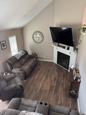 A living room with a sectional sofa, a flat-screen TV, a fireplace, and a decorative tree wall art piece.