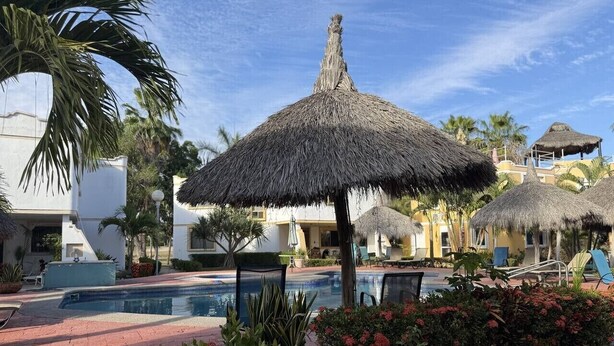 Zona de piscina amb una ombra de palla, gandules i una piscina.