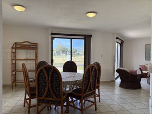 Ein Essbereich mit einem runden Tisch und Stühlen, einem Holzregal und Blick durch ein großes Fenster.