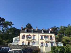 Ein großes, mehrstöckiges Gebäude mit Steinfundament, zahlreichen Fenstern mit Fensterläden und einem Balkon im zweiten Obergeschoss.