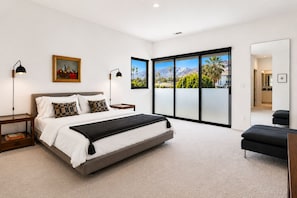 A modern bedroom with a bed, bedside tables, a painting, and a large window with a mountain view. - Downtown Modern Palm Springs Oasis | 2 King Suites (Palm Springs)