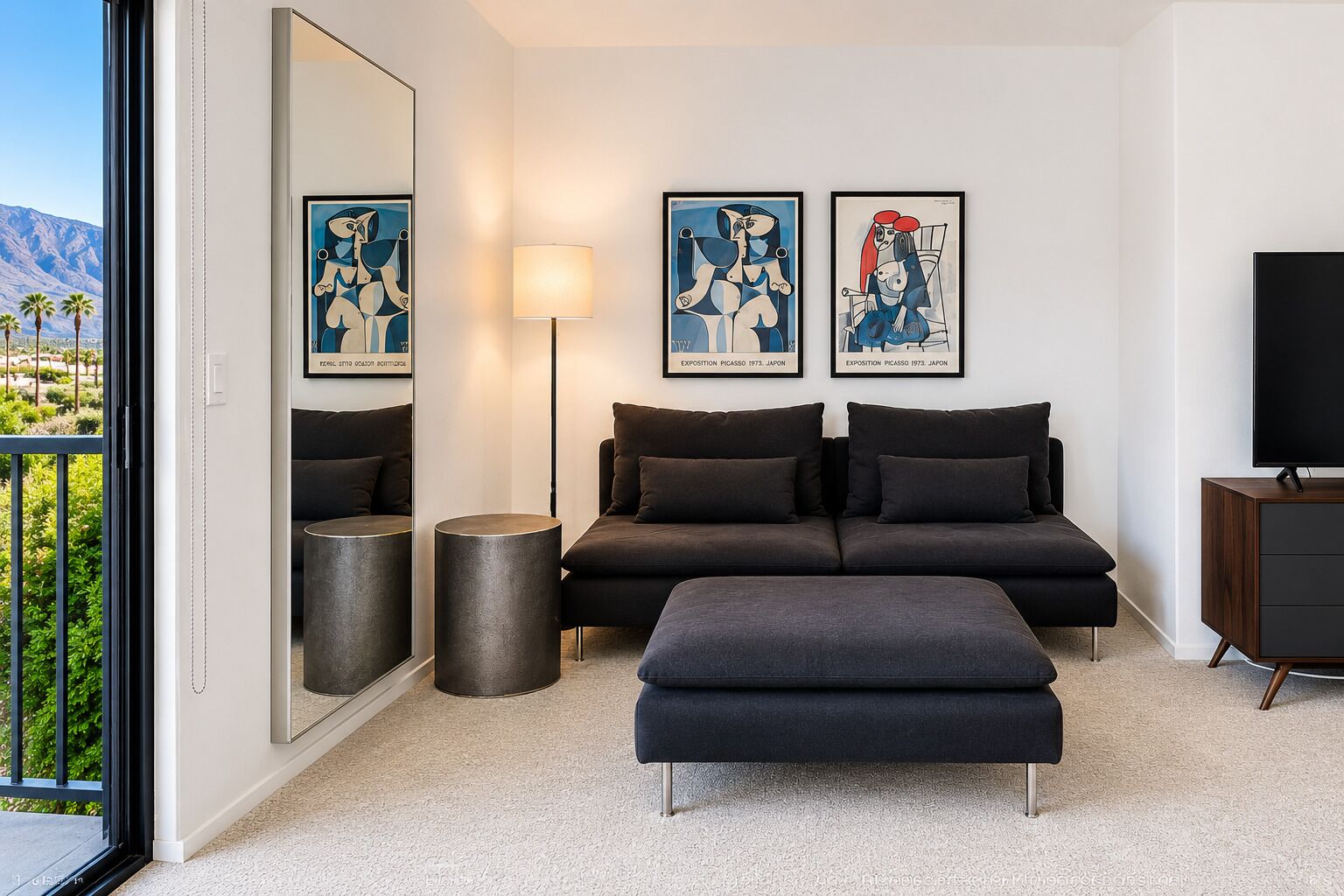 Ein modernes Wohnzimmer mit einer Couch, einem Hocker und zwei gerahmten Kunstwerken an der Wand.