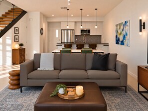 A modern living room with a sofa, a coffee table with decorative items, a staircase, a kitchen area with a microwave, and pendant lights. - Downtown Modern Palm Springs Oasis | 2 King Suites (Palm Springs)