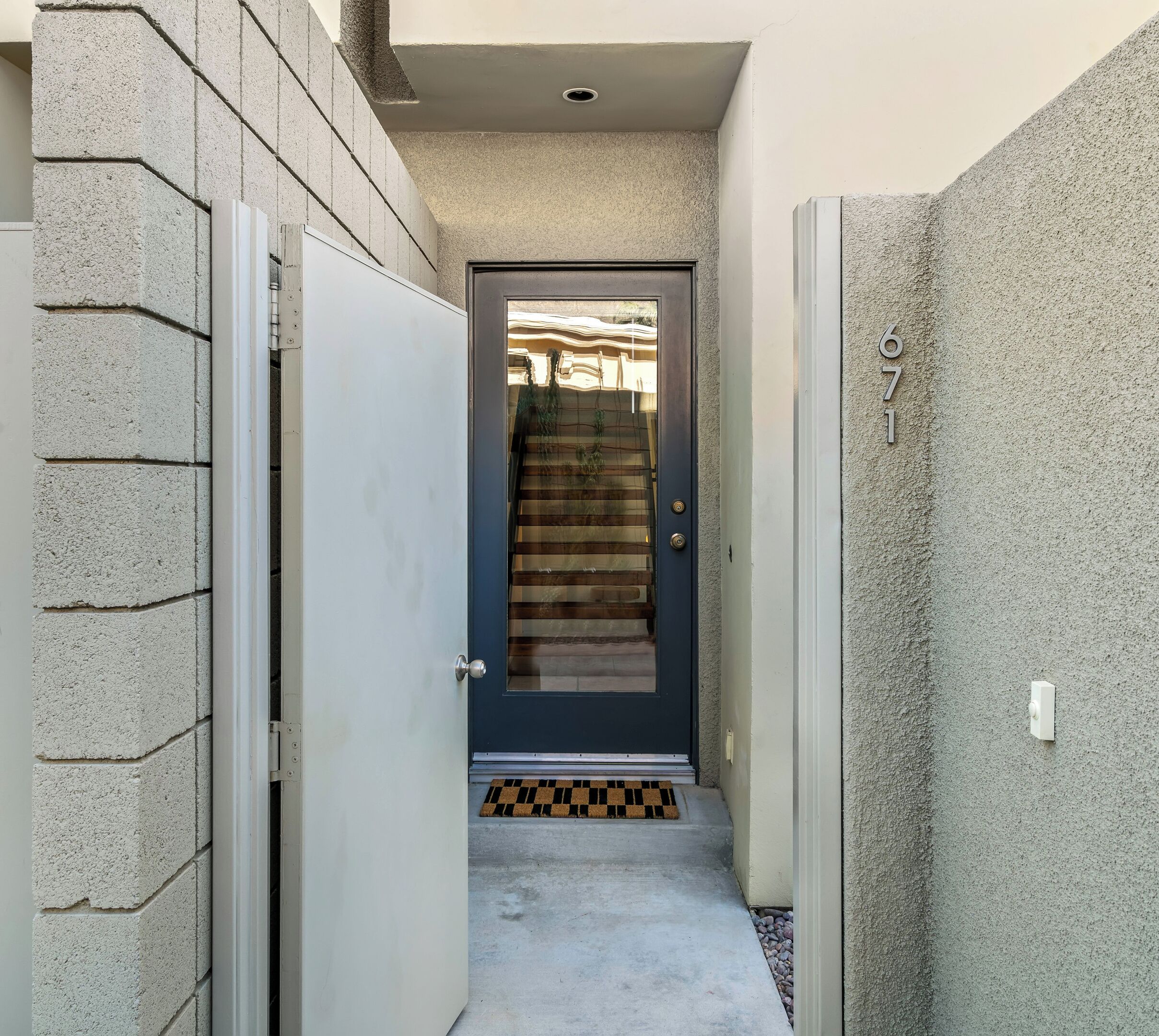 A narrow entrance with a dark door, a visible staircase, and a small doormat.