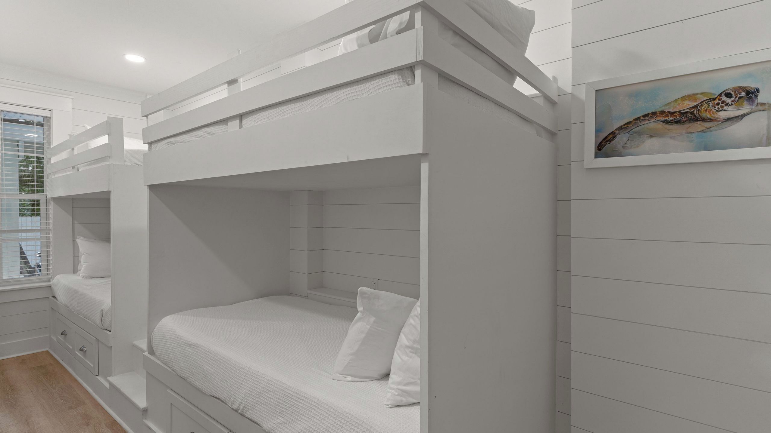 Habitación con literas, una ventana, un cuadro y suelo de madera.