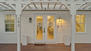 Ein Haus mit weißer Fassade, einer Doppeltür mit Glasscheiben, zwei Laternenleuchten und einem Holzboden.