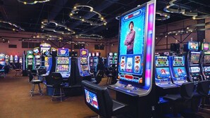 Een casino met meerdere gokkasten en een groot scherm waarop een persoon te zien is.